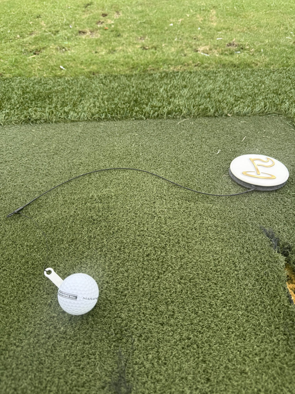 The Perfect Divot disc and steel cable laid out on a hitting mat