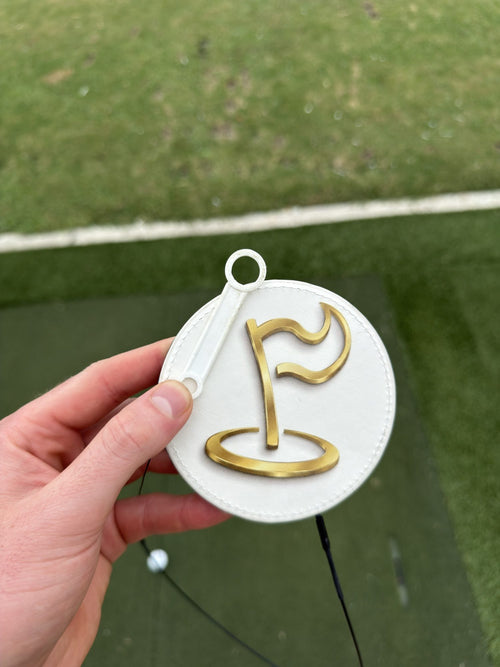 Close-up of The Perfect Divot white disc with gold flag logo