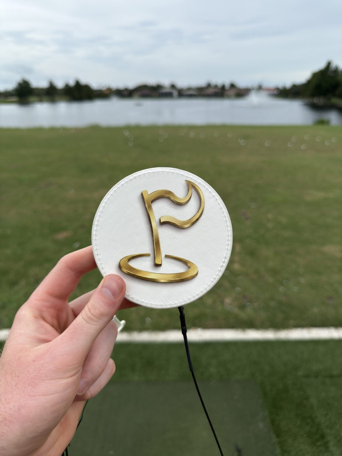 Hand holding The Perfect Divot disc at the driving range