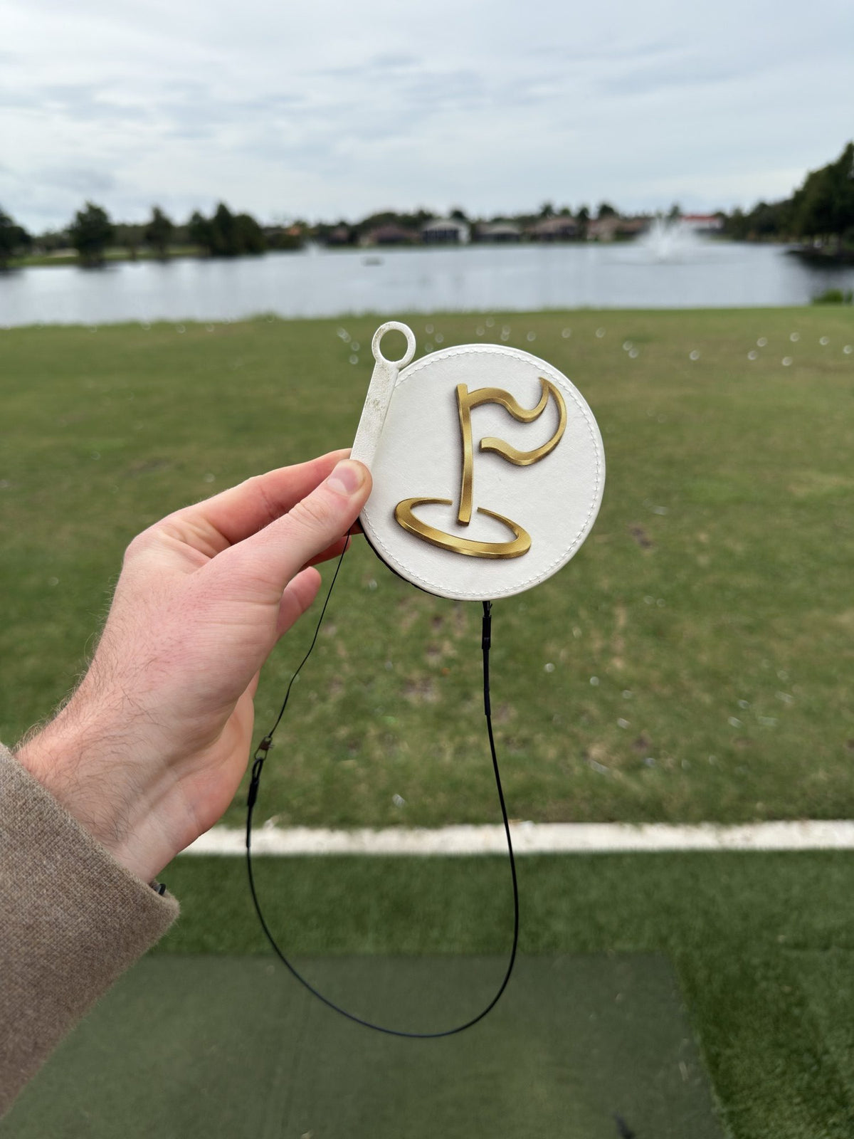 The Perfect Divot disc held up at a driving range by a lake
